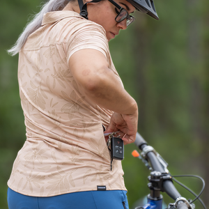 Image of the Women's Catalyst Mountain Bike Button-Down Shirt in Rhodo Tan: A high-performance jersey disguised as a stylish button-down shirt. Features a front stash pocket, built-in lens wipe, and reinforced snaps. 100% recycled with 6% Silver Ion content for natural cooling and odor control. New Tru-Fit sizing for a more feminine silhouette. UPF30 sun protection for outdoor adventures.