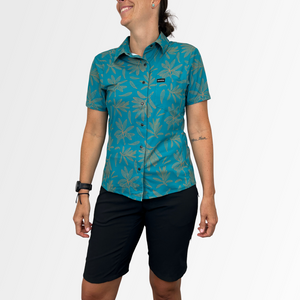 Image of the Women's Catalyst Mountain Bike Button-Down Shirt in Rhodo Teal: A high-performance jersey disguised as a stylish button-down shirt. Features a front stash pocket, built-in lens wipe, and reinforced snaps. 100% recycled with 6% Silver Ion content for natural cooling and odor control. New Tru-Fit sizing for a more feminine silhouette. UPF30 sun protection for outdoor adventures.