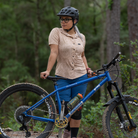 Image of the Women's Catalyst Mountain Bike Button-Down Shirt in Rhodo Tan: A high-performance jersey disguised as a stylish button-down shirt. Features a front stash pocket, built-in lens wipe, and reinforced snaps. 100% recycled with 6% Silver Ion content for natural cooling and odor control. New Tru-Fit sizing for a more feminine silhouette. UPF30 sun protection for outdoor adventures.